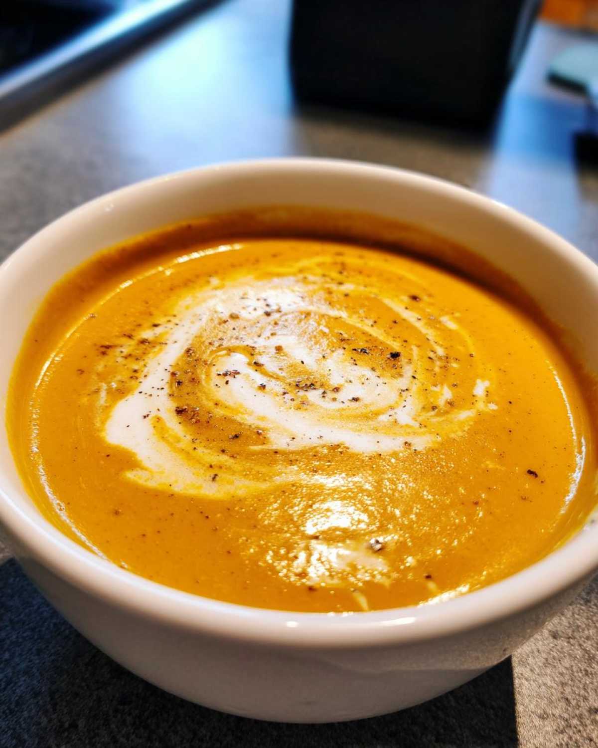 A bowl of creamy roasted butternut squash soup, swirled with cream and sprinkled with pepper.