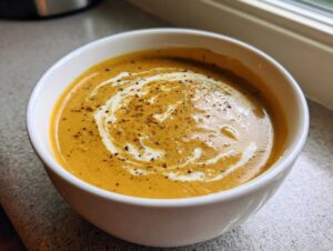 A bowl of creamy roasted butternut squash soup, swirled with cream and sprinkled with pepper.