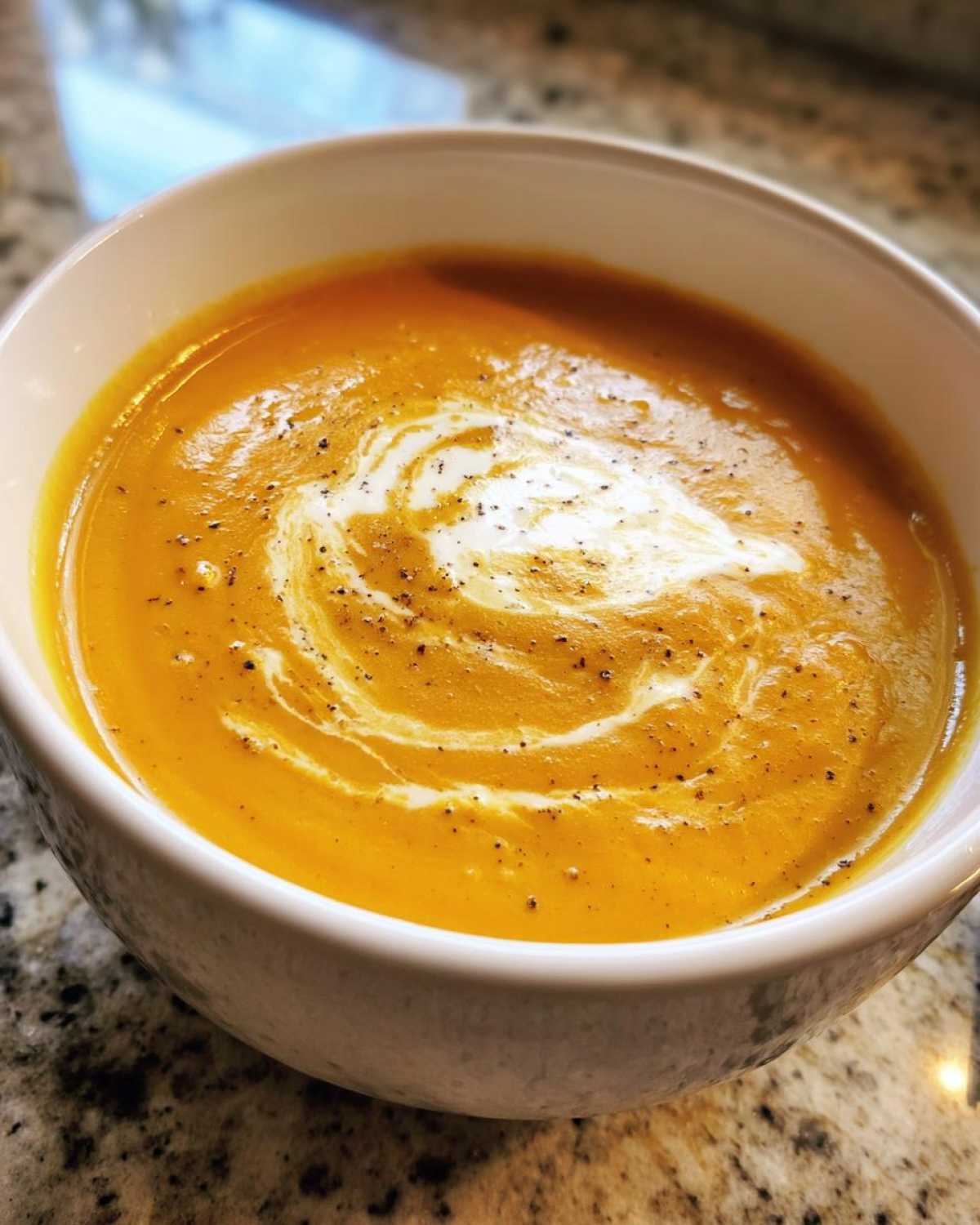 A bowl of creamy roasted butternut squash soup, swirled with cream and sprinkled with pepper.