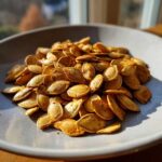 A bowl filled with crunchy roasted pumpkin seeds, glistening with oil and spices.
