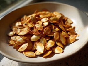A bowl filled with golden brown, crunchy roasted pumpkin seeds, seasoned and ready to eat.