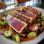 Close-up of seared ahi tuna salad with sesame-crusted tuna steaks on a bed of fresh greens and vegetables.