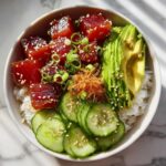 Overhead shot of a vibrant tuna poke bowl with tuna, avocado, cucumber, and rice.