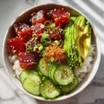 Overhead shot of a vibrant tuna poke bowl with tuna, avocado, cucumber, and rice.