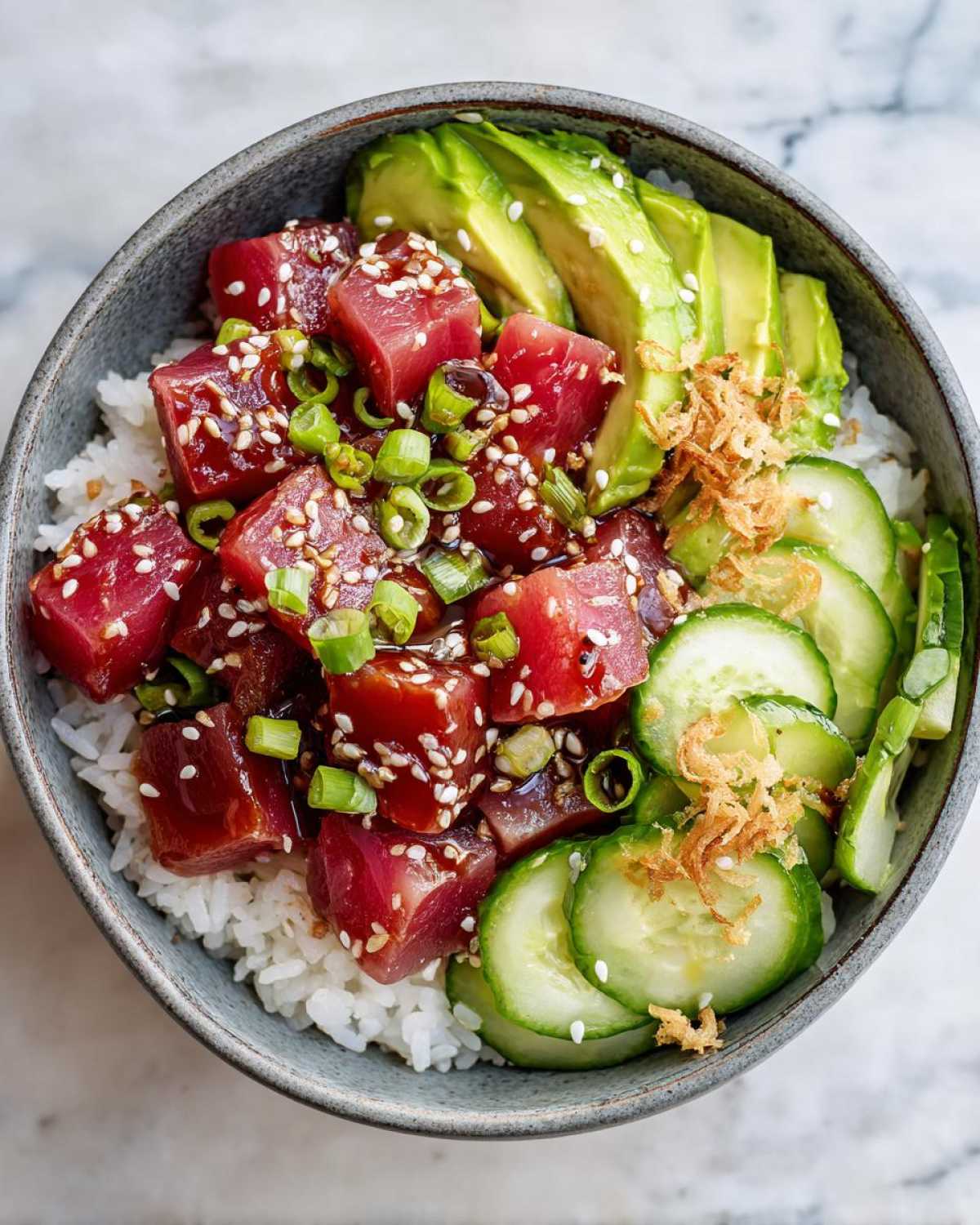 Overhead view of a vibrant tuna poke bowl with tuna, avocado, cucumber, and rice.