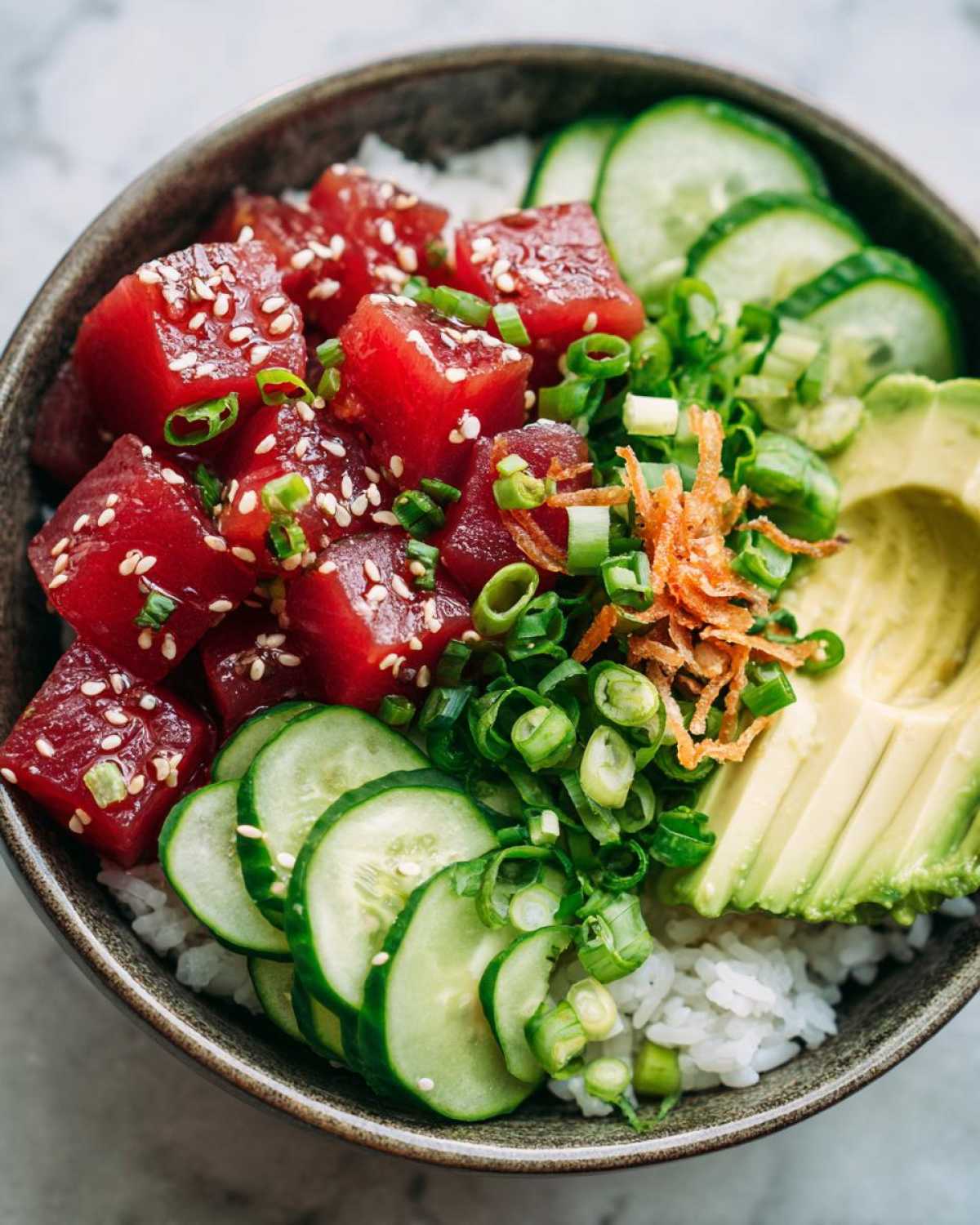 Overhead shot of a vibrant tuna poke bowl with tuna, rice, avocado, cucumber, and green onions.