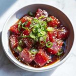 Close-up of a tuna poke bowl with tuna poke bowl marinade, sesame seeds, and green onions.