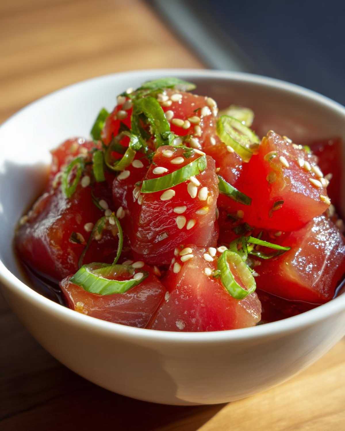 Close-up of tuna poke bowl marinade with diced tuna, sesame seeds, and green onions in a white bowl.