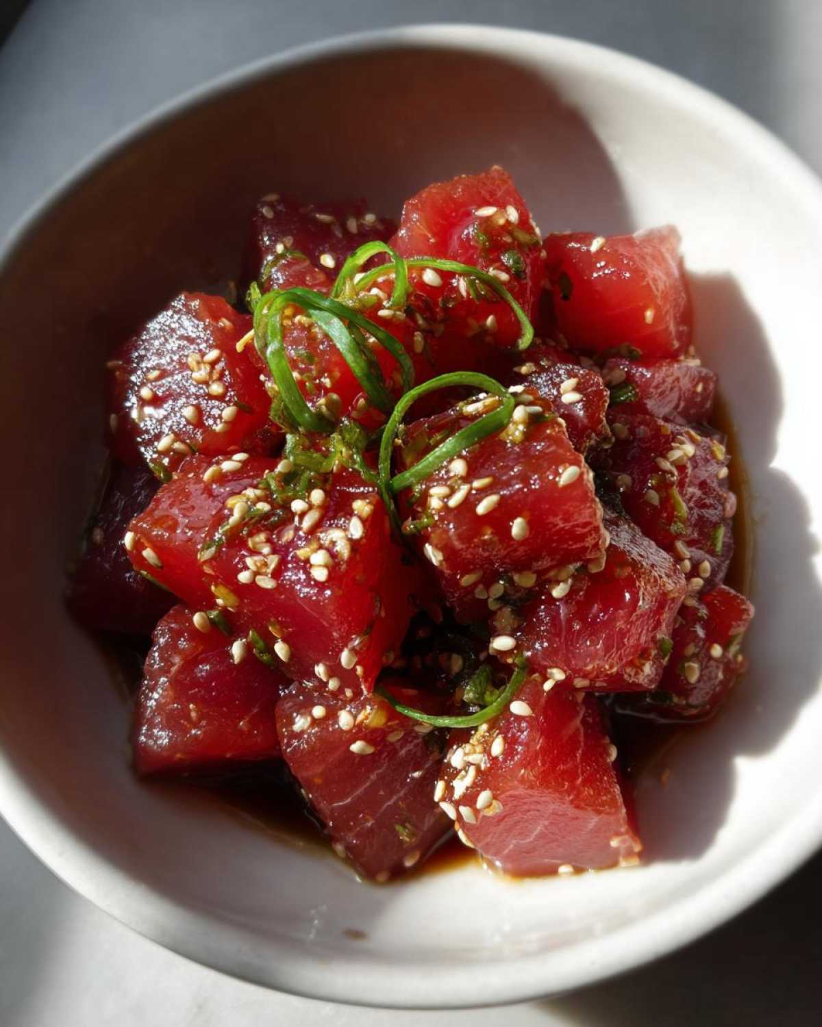 Close-up of tuna poke bowl marinade with sesame seeds and green onions in a white bowl.