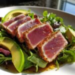 Close-up of a tuna steak salad featuring seared tuna, fresh greens, avocado slices, and a flavorful dressing.