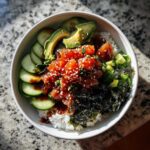 Overhead shot of a vibrant tuna sushi bowl with rice, tuna, avocado, cucumber, seaweed, and sesame seeds.