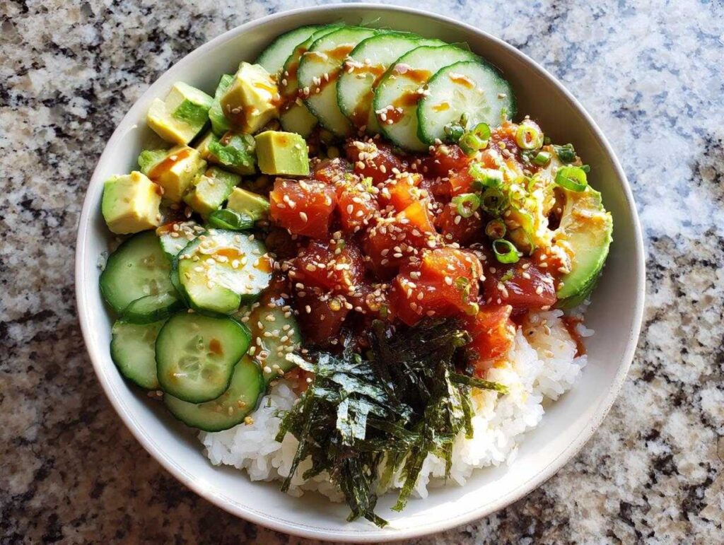 A vibrant tuna sushi bowl featuring tuna, avocado, cucumber, rice, and seaweed, topped with sesame seeds.
