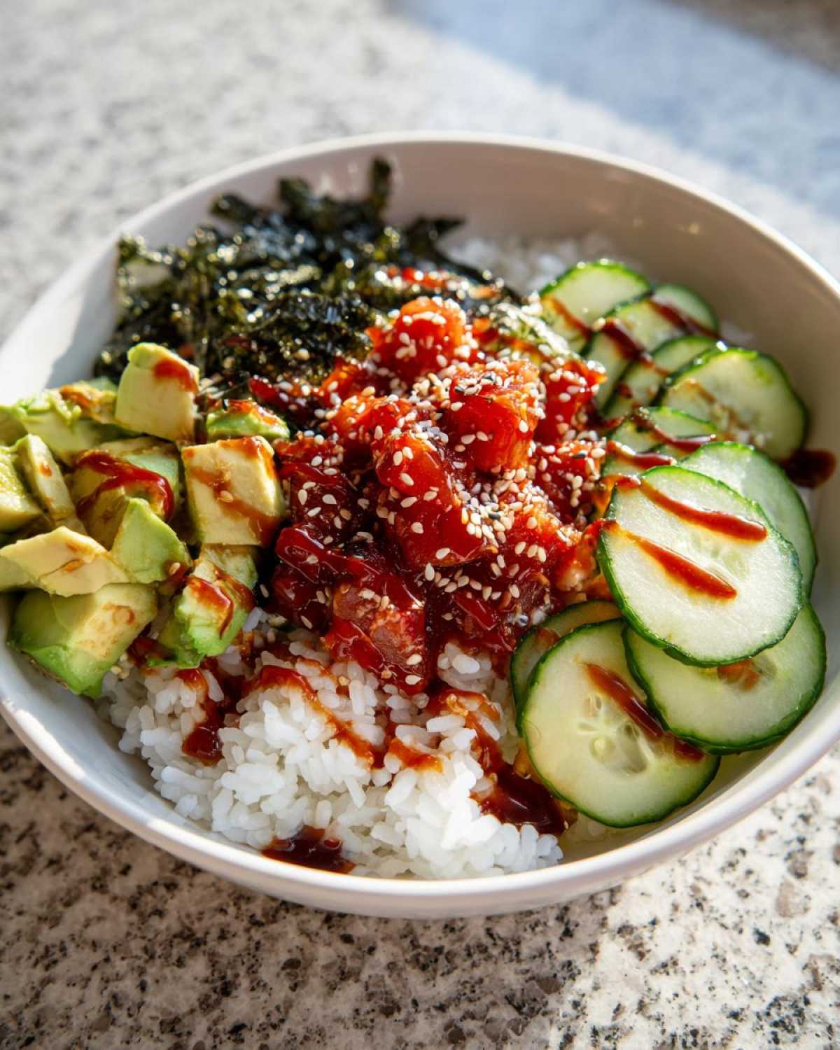 A vibrant tuna sushi bowl with tuna, rice, avocado, cucumber, and seaweed, drizzled with sauce.