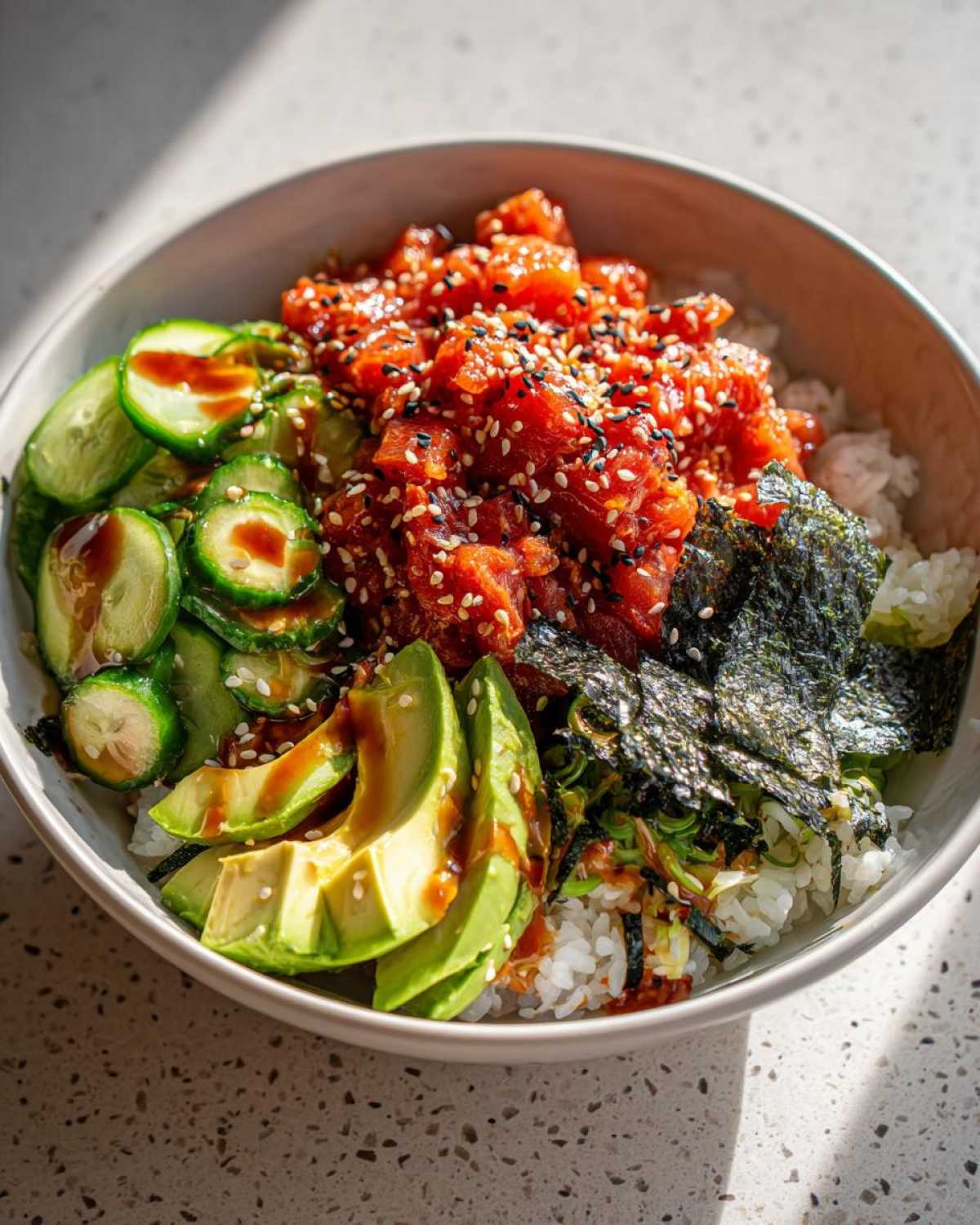 A vibrant tuna sushi bowl filled with rice, tuna, avocado, cucumber, and seaweed.
