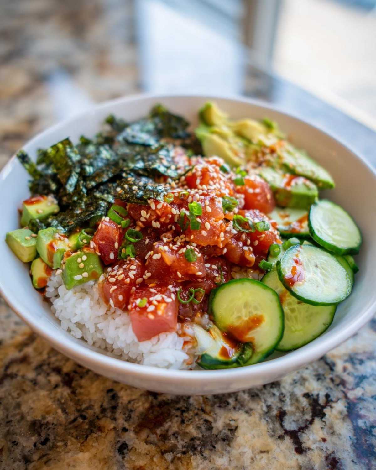 A vibrant tuna sushi bowl with tuna, rice, avocado, cucumber, and seaweed, sprinkled with sesame seeds.
