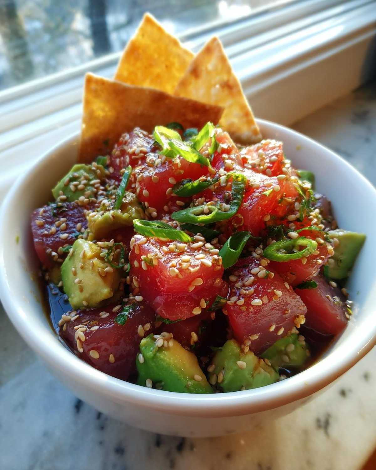 A bowl of fresh tuna tartare with avocado, sesame seeds, and green onions, served with tortilla chips.
