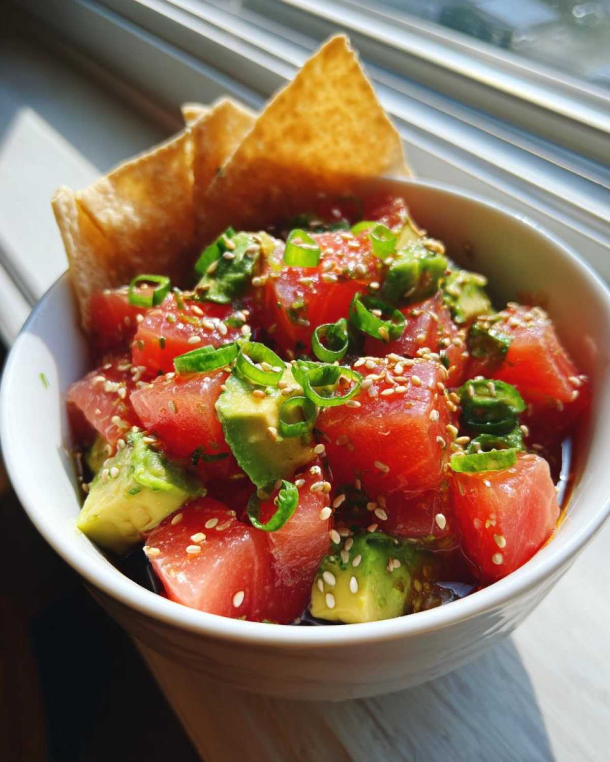Close-up of a tuna tartare bowl with diced tuna, avocado, sesame seeds, and green onions.