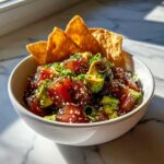 A bowl of fresh tuna tartare with avocado, sesame seeds, and green onions, served with tortilla chips.