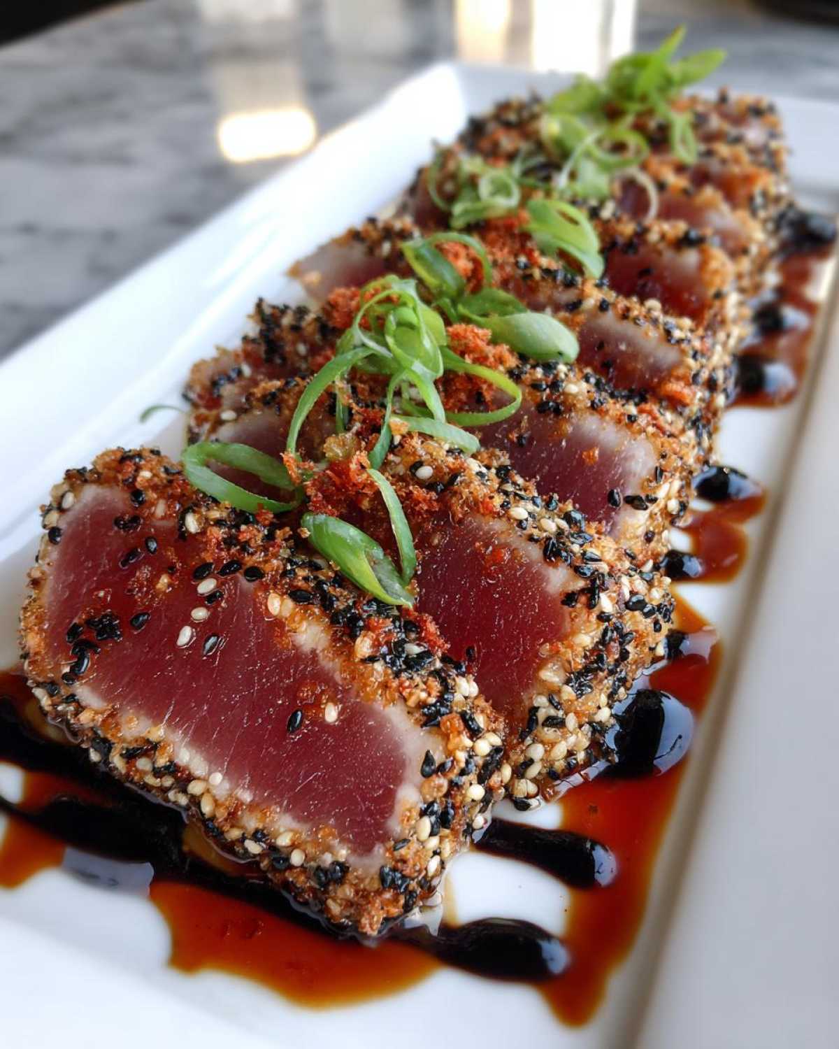 Slices of tuna tataki crusted with sesame seeds, garnished with scallions and sauce on a white plate.