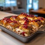 Close-up of freshly baked turkey cranberry sliders in a baking pan, topped with poppy seeds and cranberry sauce.