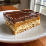A close-up of a decadent Twix cookie bar with a shortbread base, gooey caramel, and chocolate topping.
