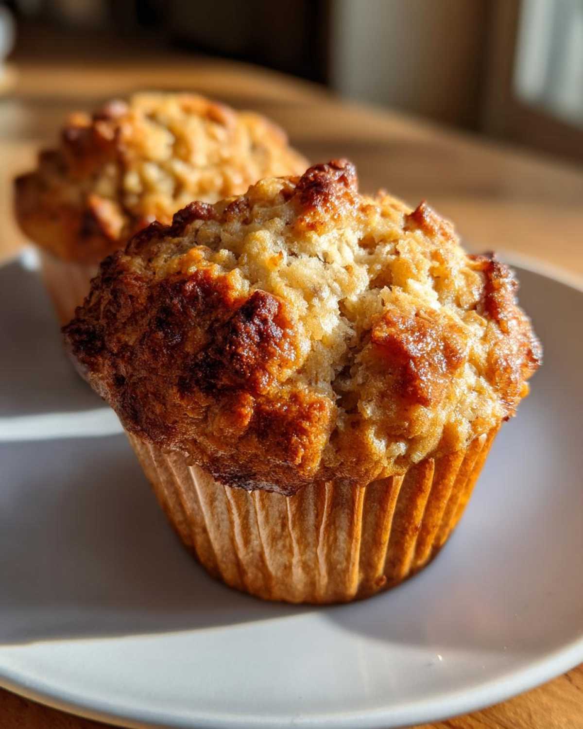 Close-up of two moist 3-ingredient banana muffins on a white plate, with golden-brown tops.