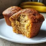 Close-up of a moist 3-ingredient banana muffin with a bite taken out, showing its fluffy texture.