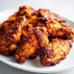 A plate of perfectly cooked crispy air fryer chicken wings with a golden-brown, seasoned coating.