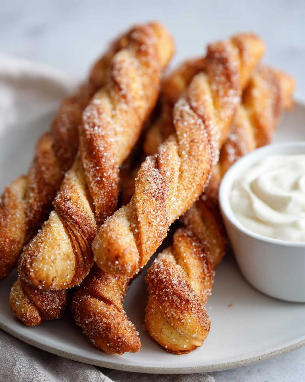 Close-up of golden-brown air fryer cinnamon twists coated in sugar and cinnamon, served with a side of creamy dip.