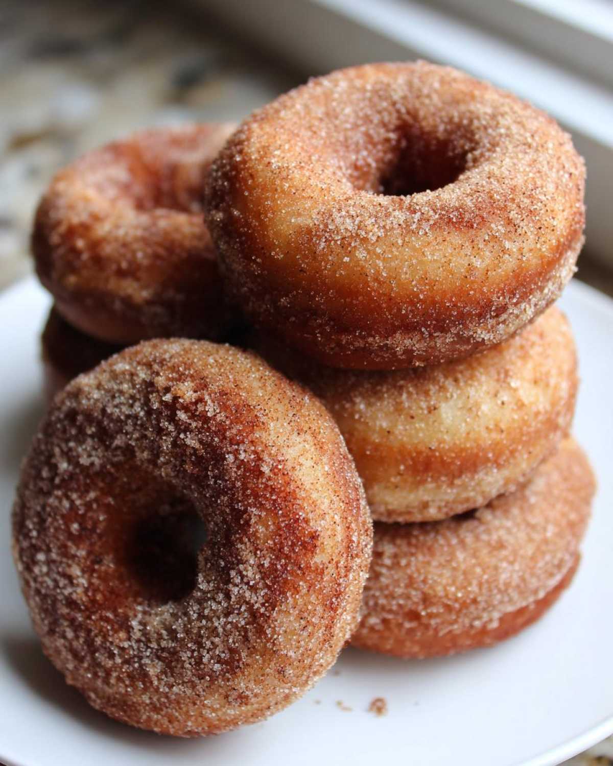 A close-up view of a stack of freshly baked apple cider donuts, coated in cinnamon sugar.