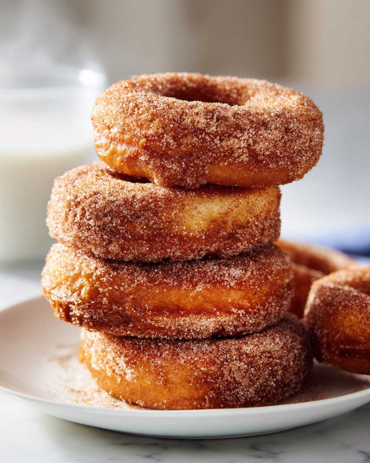 A close-up stack of freshly baked apple cider donuts coated in cinnamon sugar.