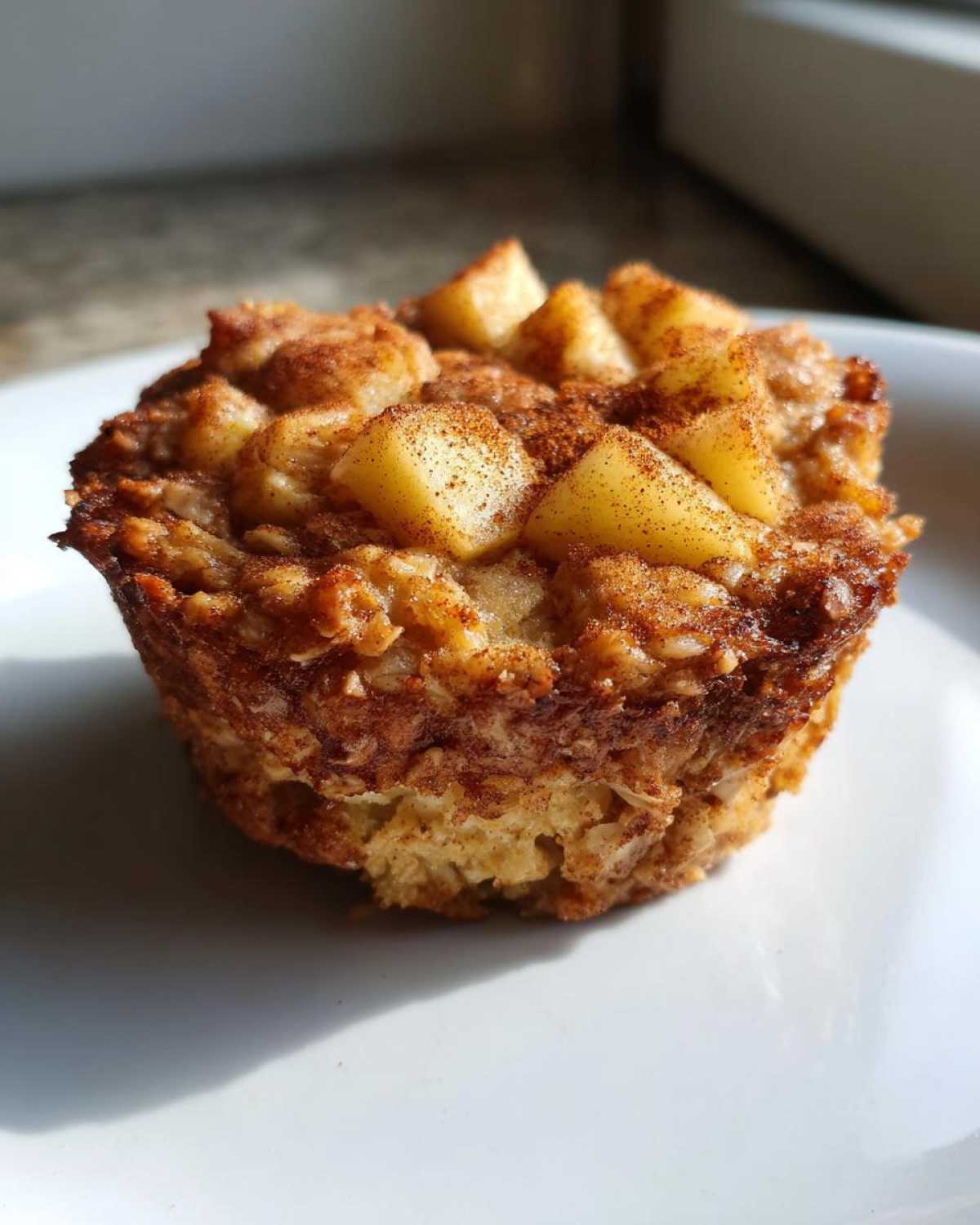 A close-up of a baked apple cinnamon oatmeal cup topped with diced apples and cinnamon.