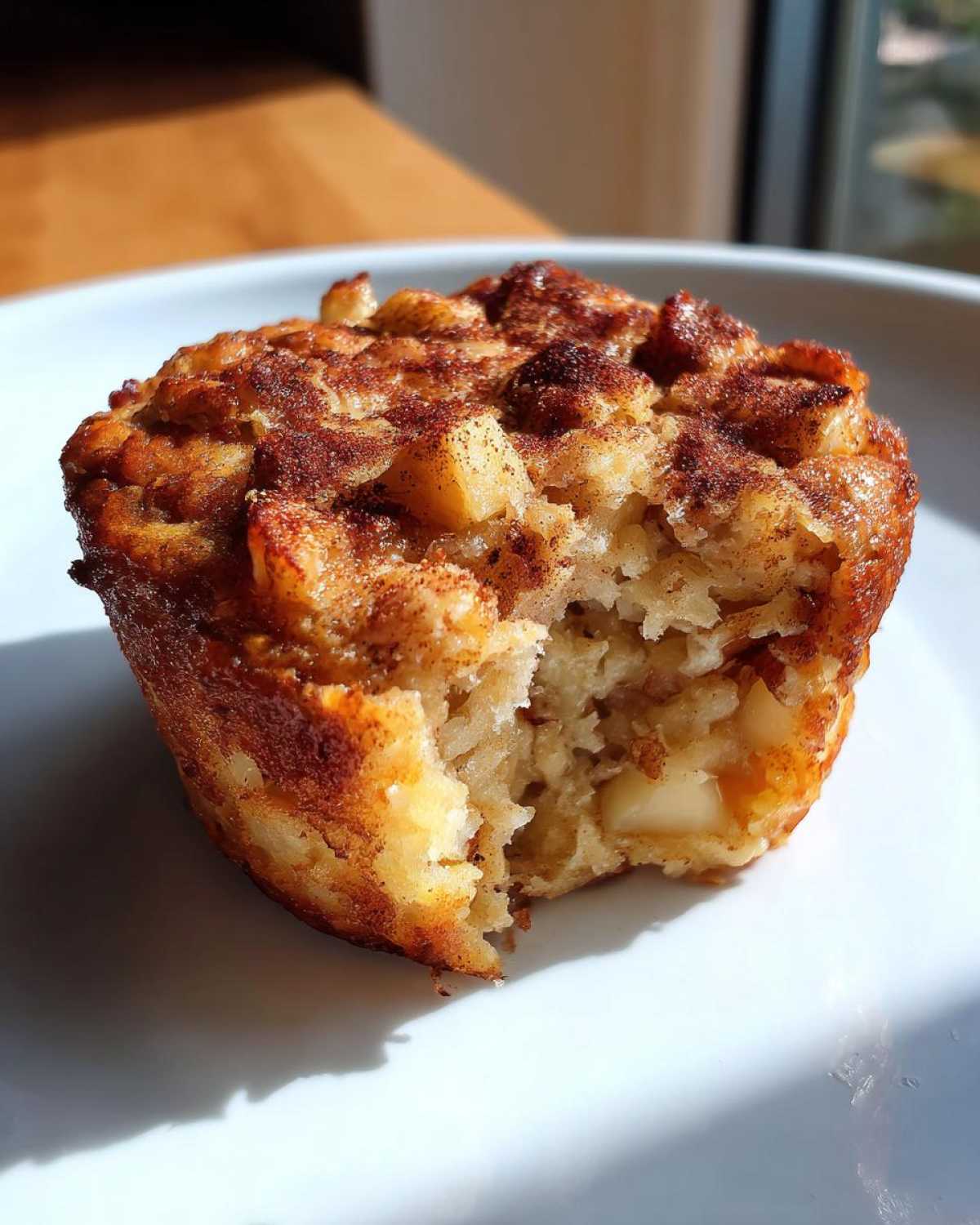 A bite taken out of a golden-brown apple cinnamon oatmeal cup, showing the soft interior with apple chunks.