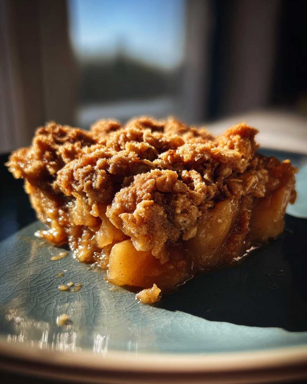 A close-up of a slice of apple crisp with oats on a blue plate, showing tender baked apples and a crumbly oat topping.