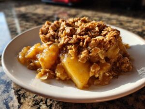 A close-up of a slice of apple crisp with oats on a white plate, featuring tender baked apples and a crunchy oat topping.