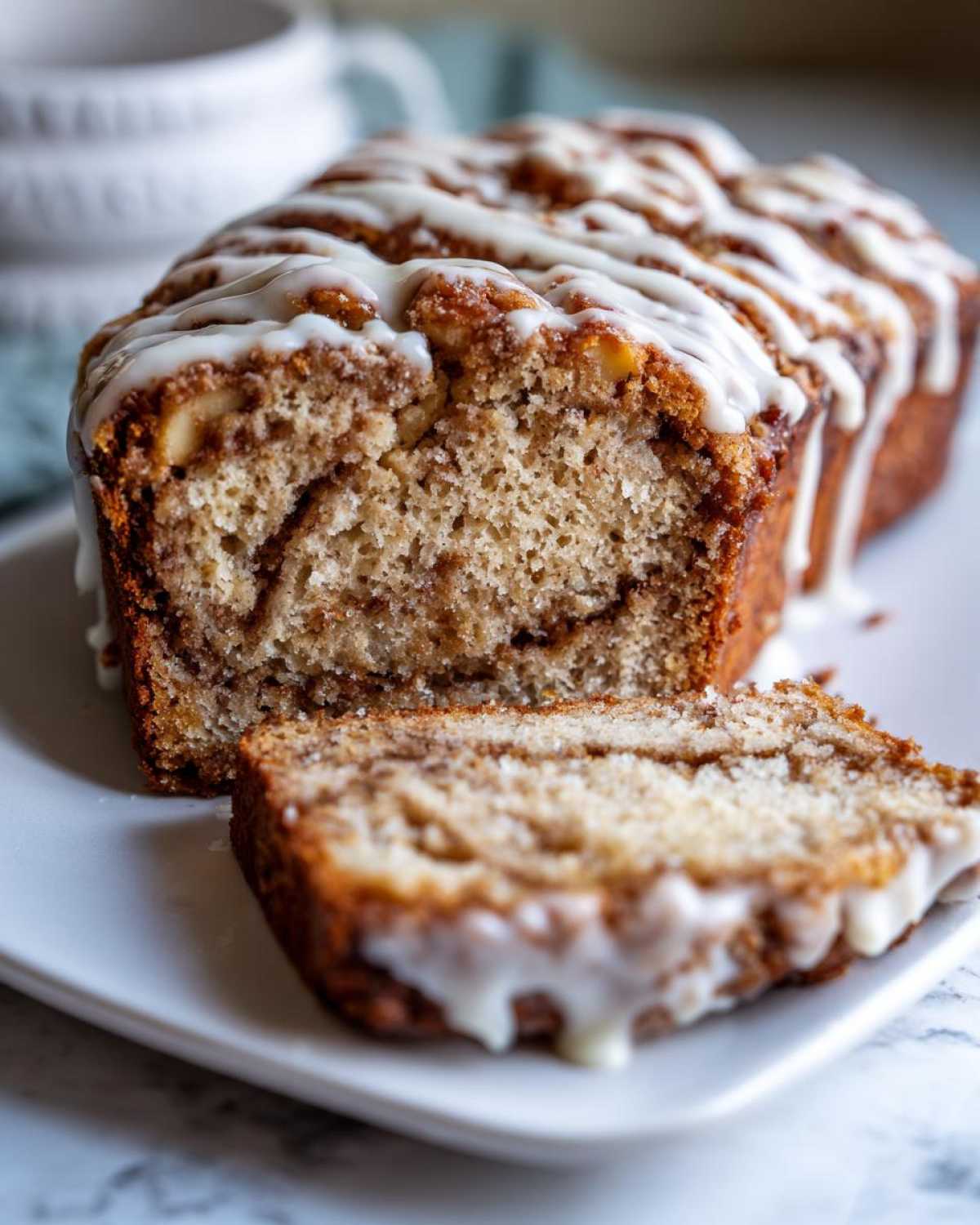 A slice of moist apple fritter bread with a cinnamon swirl and drizzled with white glaze.