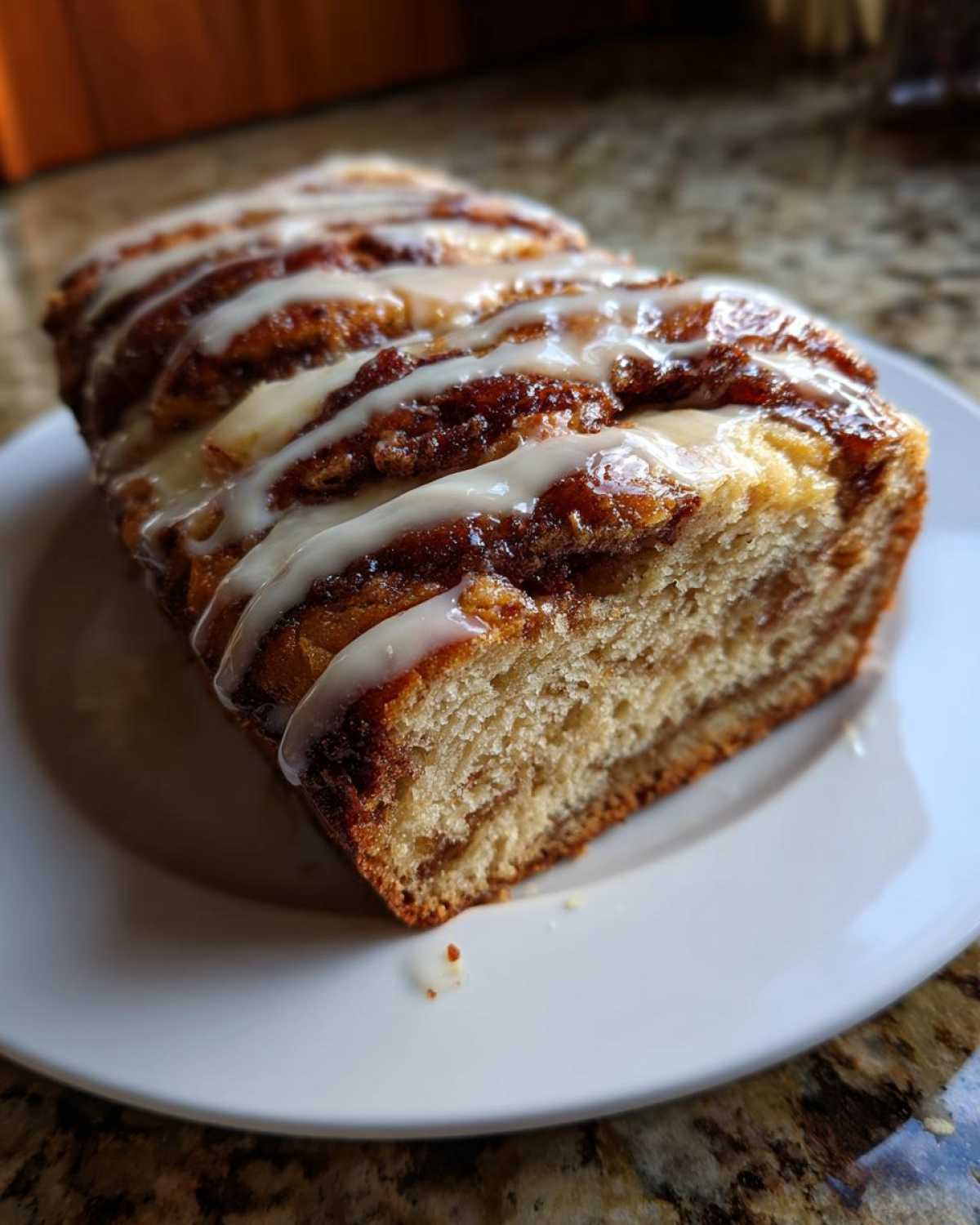 A slice of moist apple fritter bread with cinnamon swirls and a sweet glaze on a white plate.