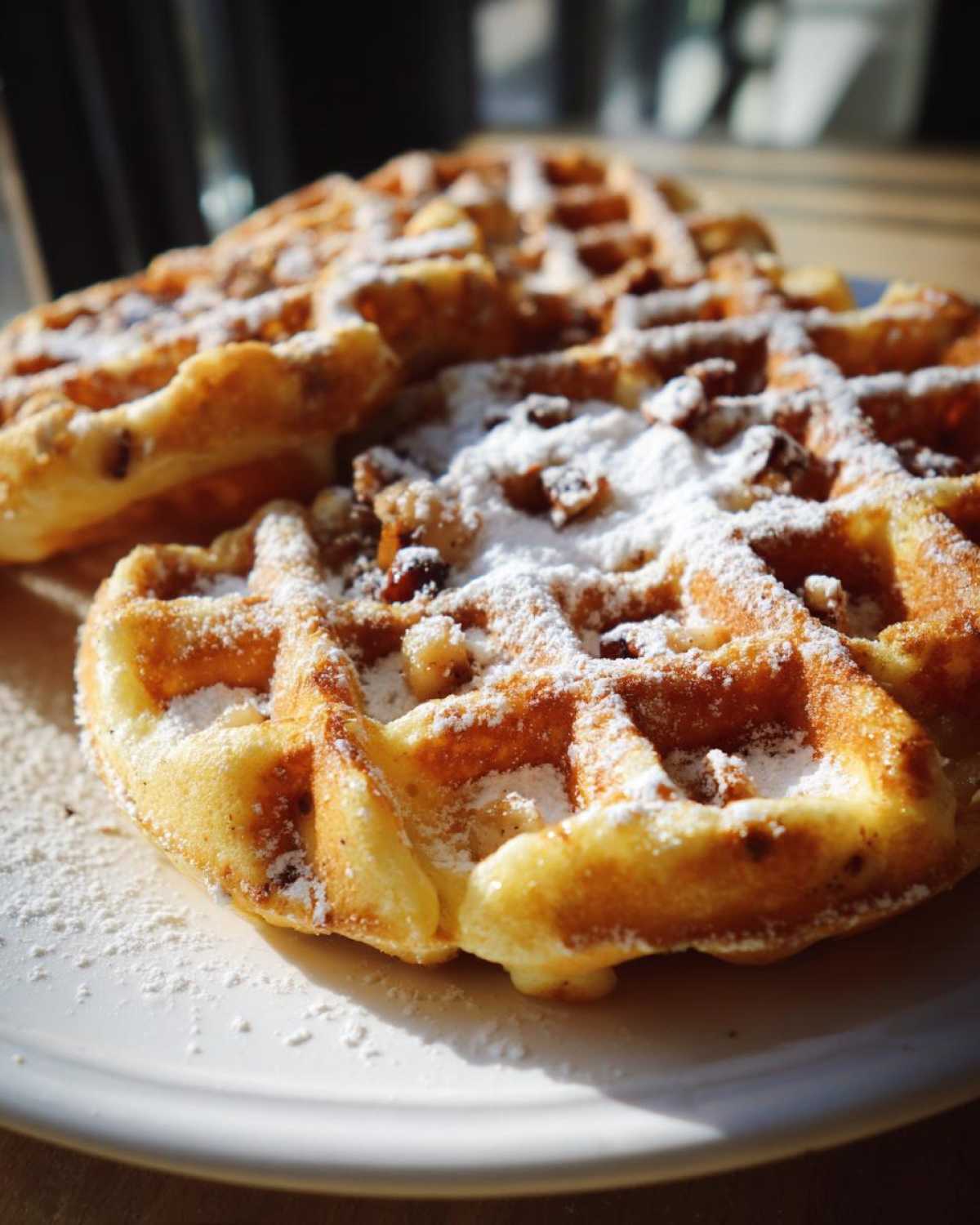 Close-up of golden brown apple fritter waffle donuts dusted with powdered sugar and nuts.