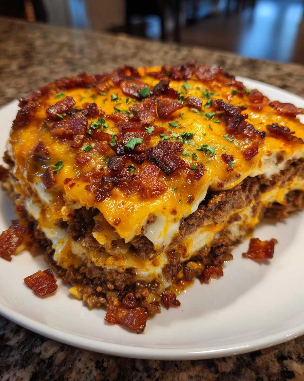 A slice of delicious bacon cheeseburger lasagna on a white plate, topped with melted cheese and crumbled bacon.
