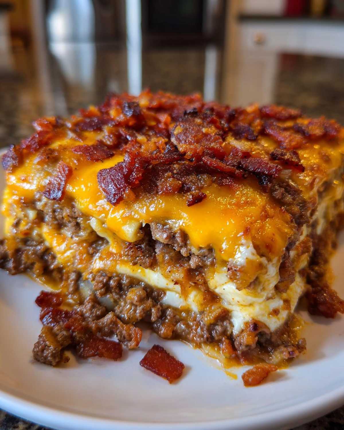 A close-up of a slice of bacon cheeseburger lasagna, featuring layers of ground beef, cheese, and crispy bacon.