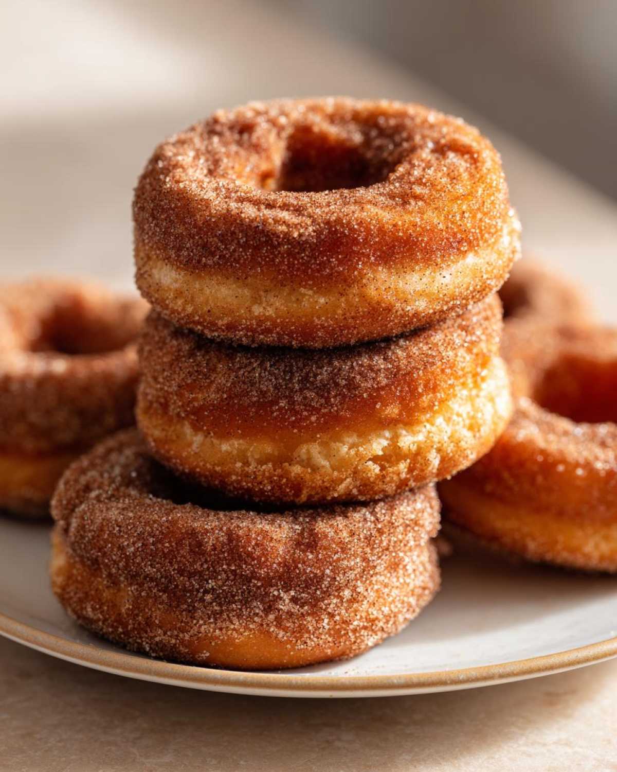 A close-up of a stack of freshly baked apple cider donuts coated in cinnamon sugar.