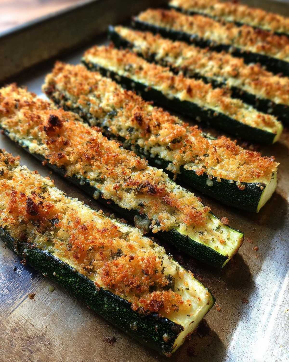 Close-up of baked zucchini halves topped with crispy breadcrumbs and herbs.