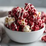 A white bowl filled with bloody red velvet popcorn drizzled with white chocolate.