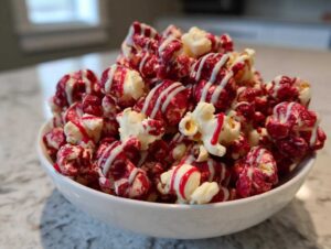 A close-up of a white bowl filled with bloody red velvet popcorn drizzled with white icing.