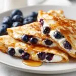 Close-up of a blueberry breakfast quesadilla, filled with cream cheese and blueberries, drizzled with syrup.