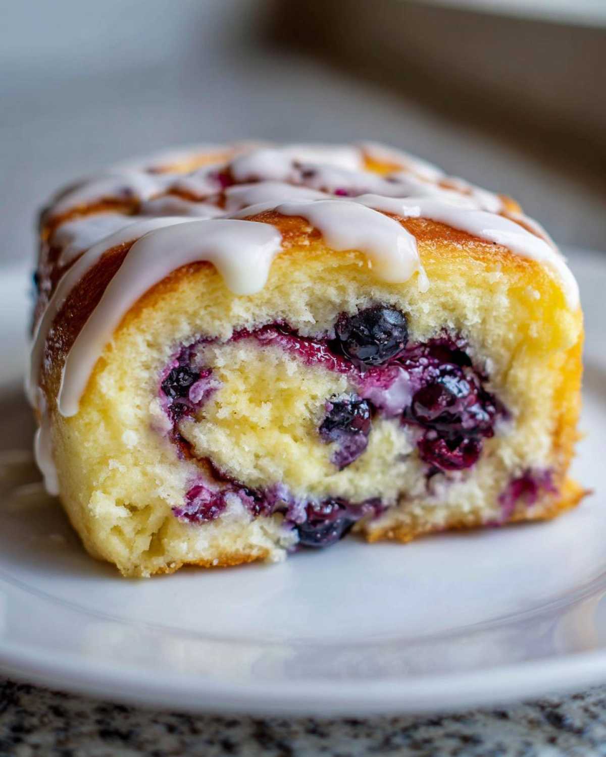 A single blueberry cheesecake roll drizzled with white glaze, showcasing the swirl and juicy blueberries inside.