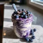 Close-up of creamy blueberry overnight oats in a mason jar, topped with fresh blueberries and chocolate shavings.
