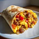 A close-up of a hearty breakfast burrito packed with scrambled eggs, sausage, and colorful bell peppers.