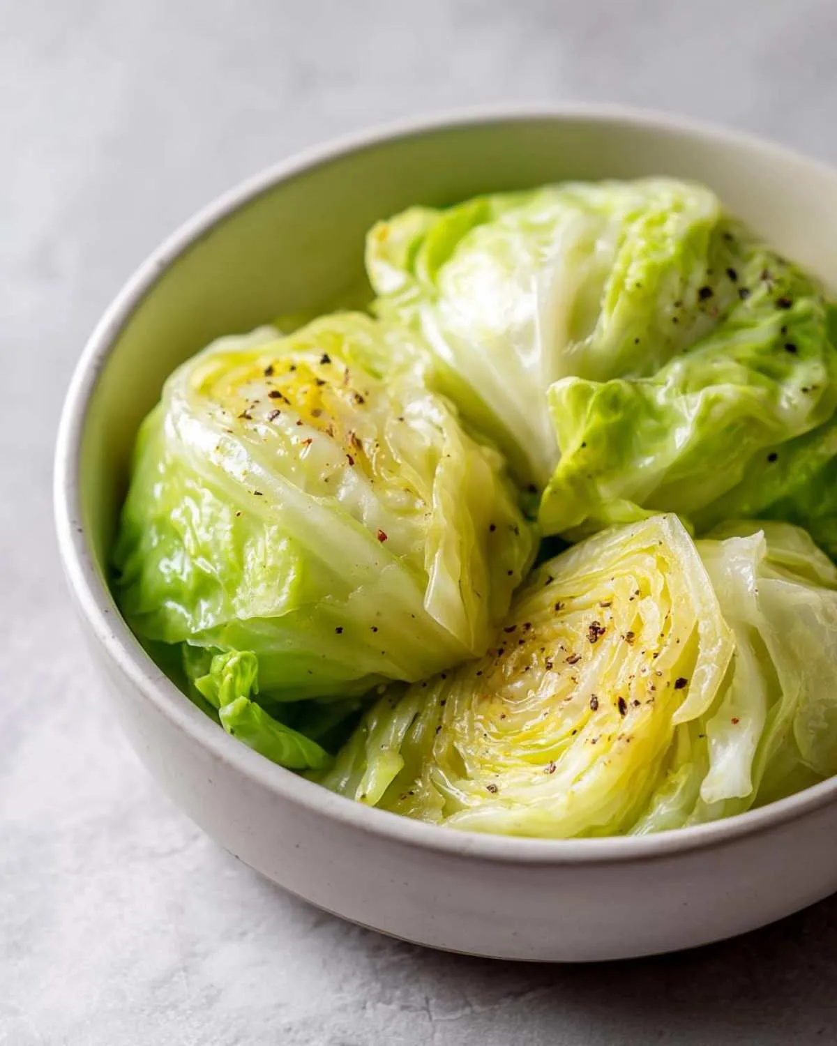 Close-up of a bowl filled with tender, seasoned cabbage boil wedges, seasoned with pepper.