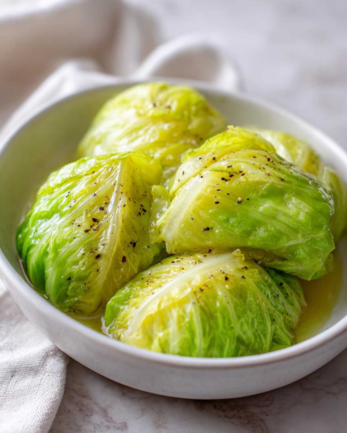 Close-up of a white bowl filled with tender cabbage boil, seasoned with pepper.